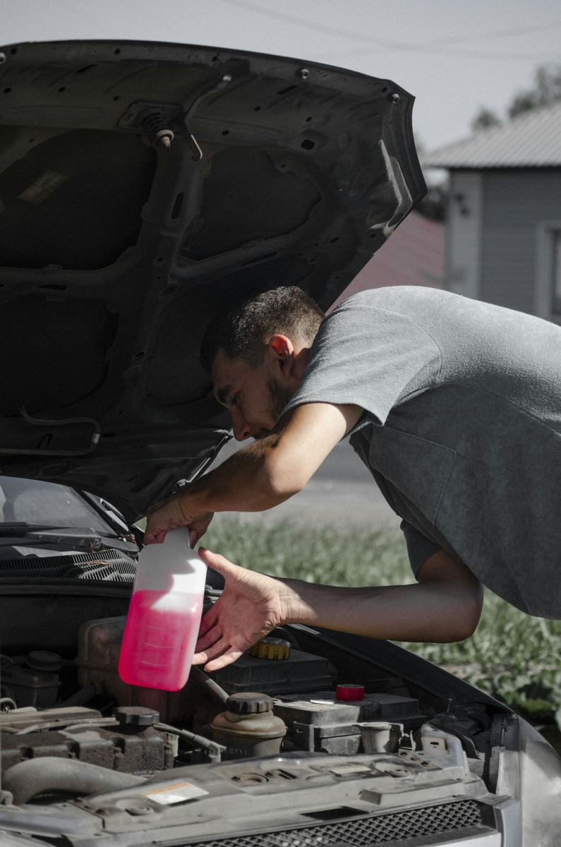 Mechanic topping up coolant under an open hood